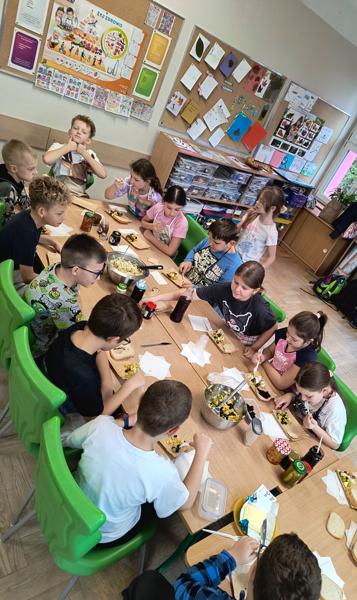 Grupa uczniów przy stole, na którym znajdują się zdrowe potrawy.