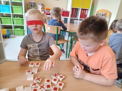 Chłopiec z opaską na oczach rozpoznaje klocki za pomocą dotyku, drugi chłopiec sprawdza czy dobrze to robi