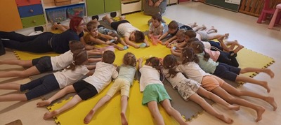 Grupa dzieci w strojach gimnastycznych leży na brzuchu i ćwiczy z woreczkiem foliowym