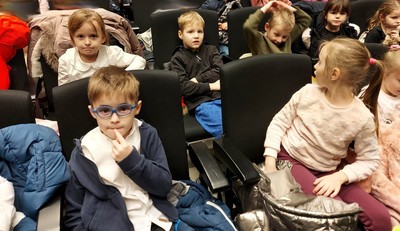 Dzieci siedzą na fotelach w teatrze i czekają na przedstawienie