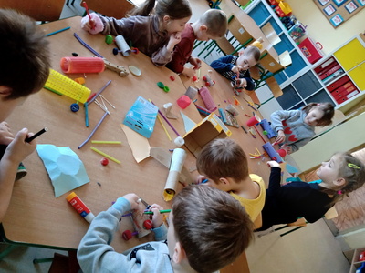 Stół z materiałami z recyklingu i dzieci budujące z nich samochody