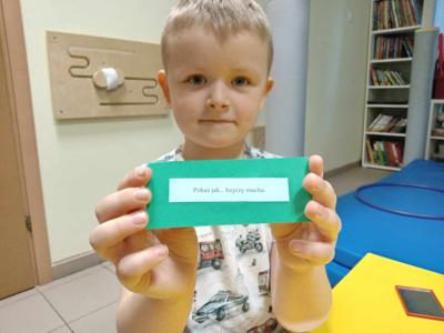 P-pokaż jak... chłopiec trzyma karteczkę z zadaniem logopedycznym