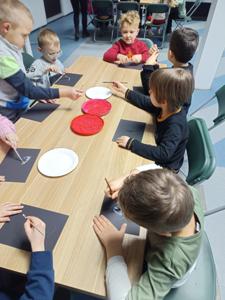 Dzieci przy stole wyklejają serduszka kolorowym ryżem.