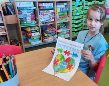 Dziewczynka trzyma kartę pracy związaną z autyzmem