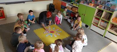 Dzieci wraz z nauczycielką siedzą na macie. 