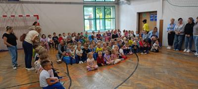 Grupa dzieci siedzi na sali gimnastycznej.