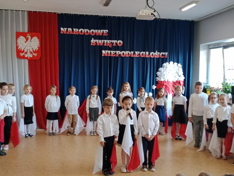 Troje dzieci ubranych na galowo występuje przed przedszkolakami