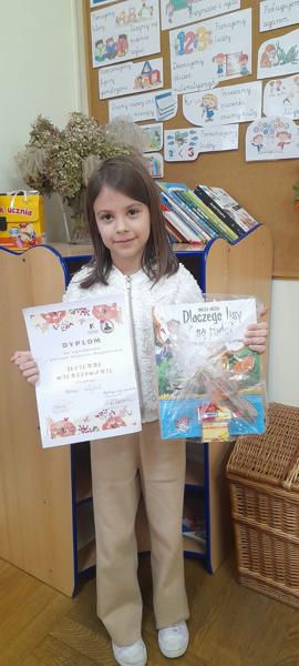 Helenka prezentuje dyplom i nagrodę książkową.