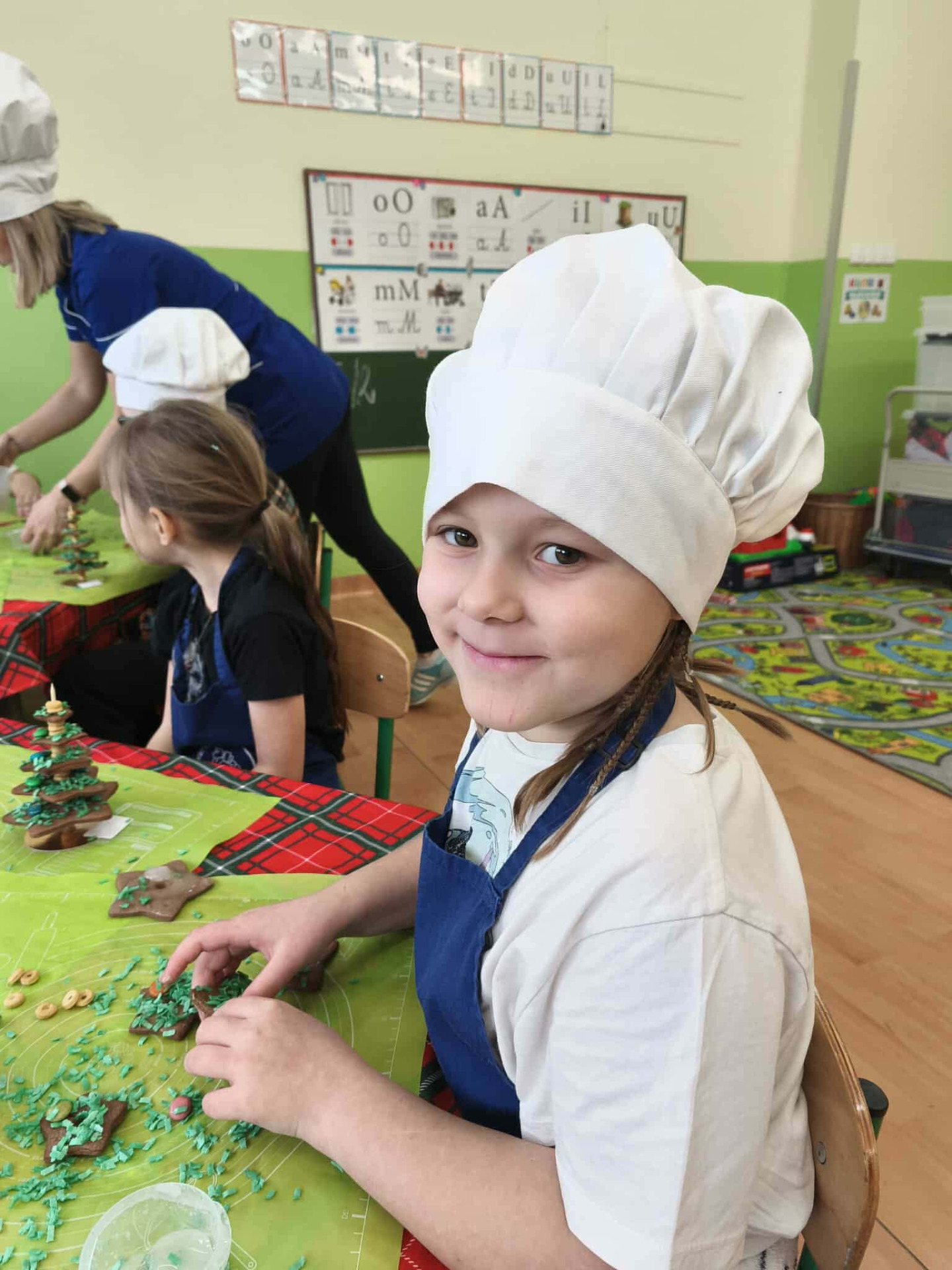 Uczennica w kucharskiej czapce dekoruje pierniczki.