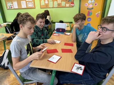 Uczniowie klasy siódmej siedzą przy stolikach i grają w memory z wynalazkami.