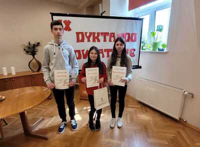 Reprezentanci naszej szkoły podczas  konkursu o tytuł: "Mistrza Ortografii Powiatu Łódzkiego Wschodniego". Uczniowie stoją na tle planszy z napisem IX DYKTANDO POWIATOWE i trzymają dyplomy. 