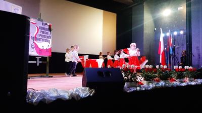 Grupa przedszkolaków ubrana na biało czerwono stoi na scenie 