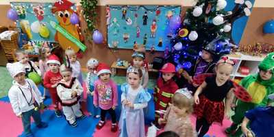 Grupka dzieci przebranych w stroje karnawałowe stojąca na tle niebieskiej tablicy z balonami