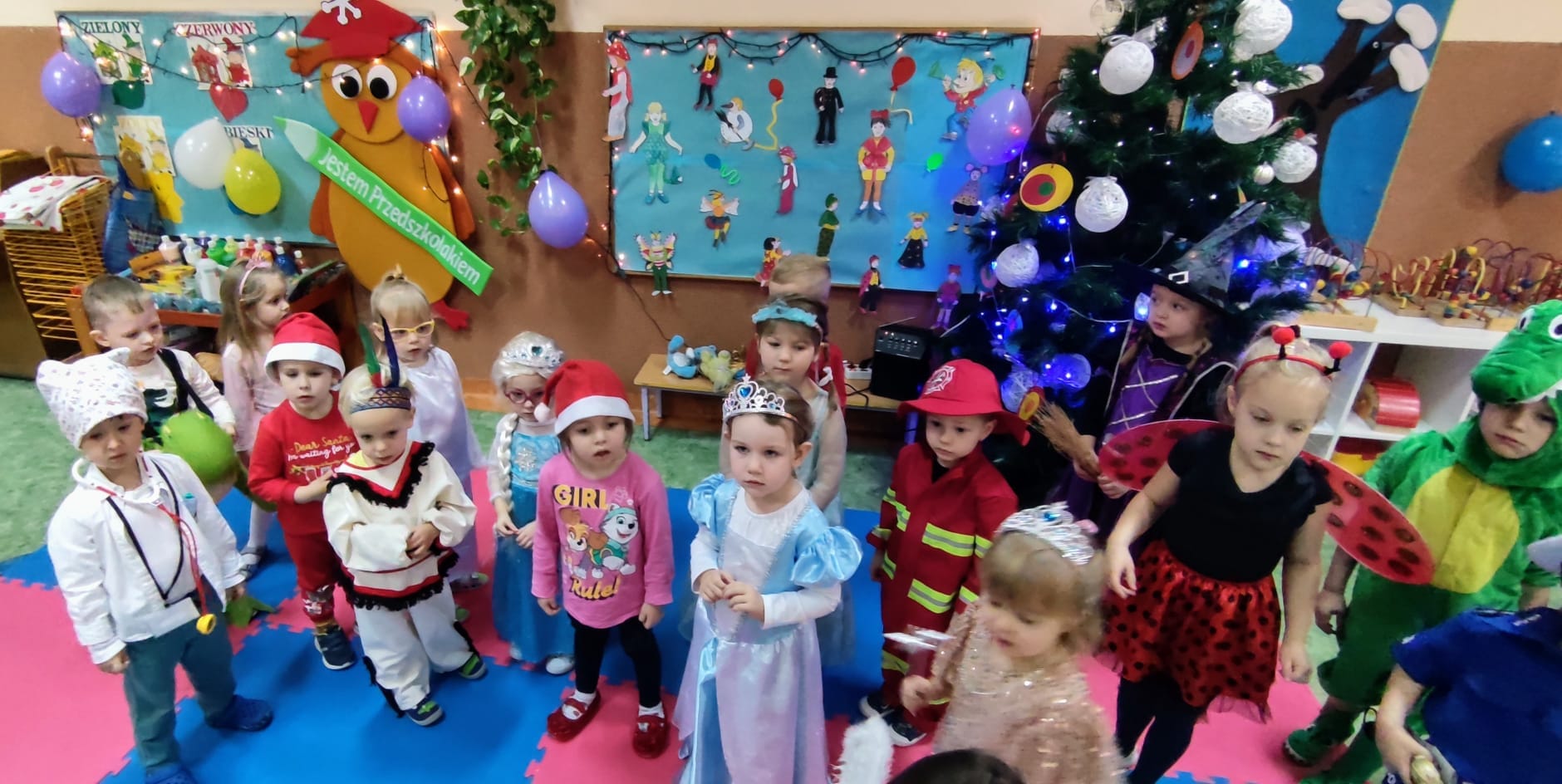 Grupka dzieci przebranych w stroje karnawałowe stojąca na tle niebieskiej tablicy z balonami