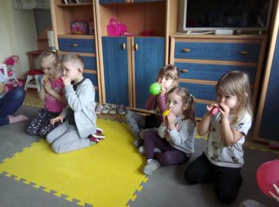 Pięcioro dzieci siedzi na macie i nadmuchuje kolorowe balony.