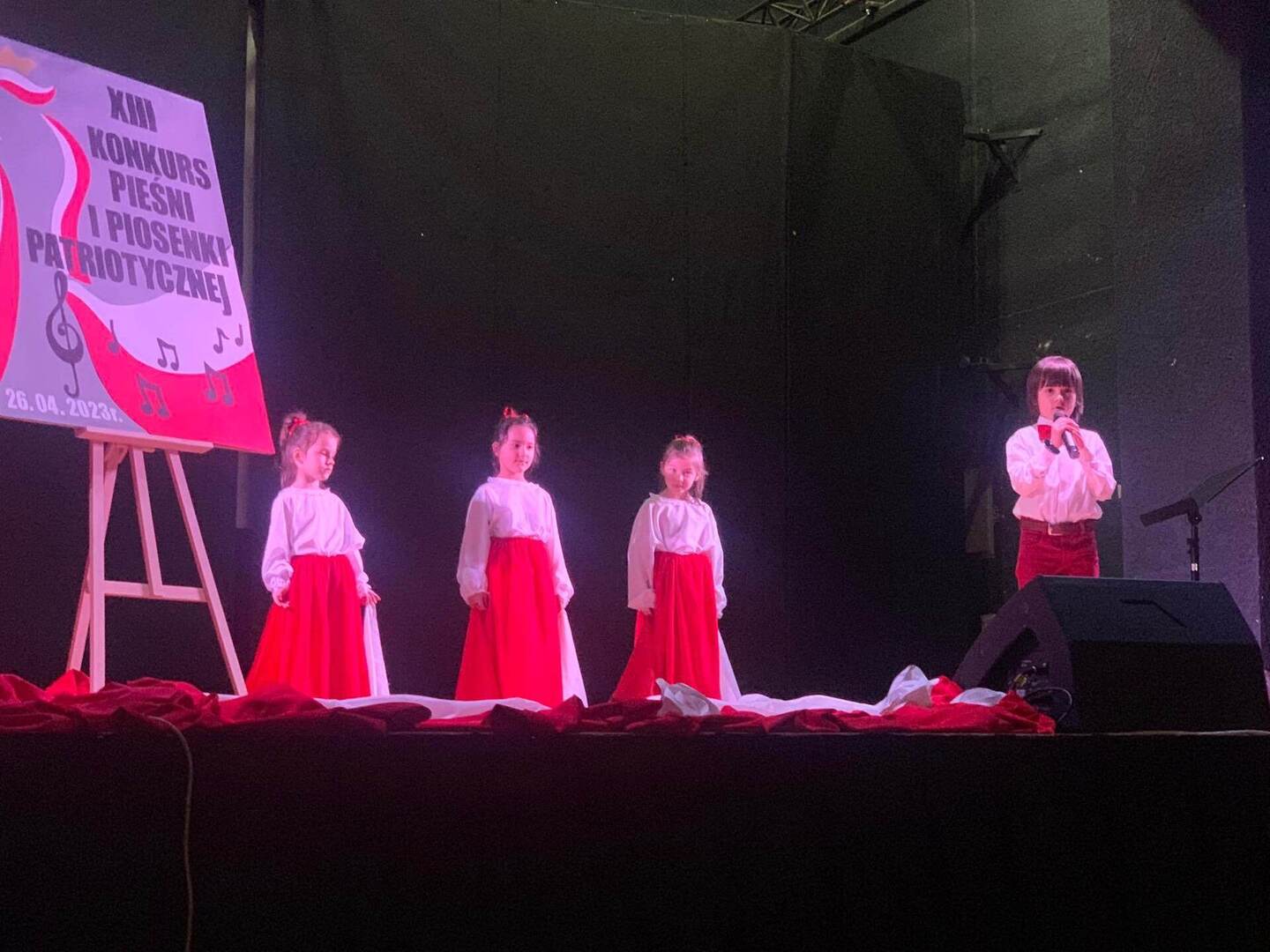 Solista oraz trzy dziewczynki w biało-czerwonych strojach.