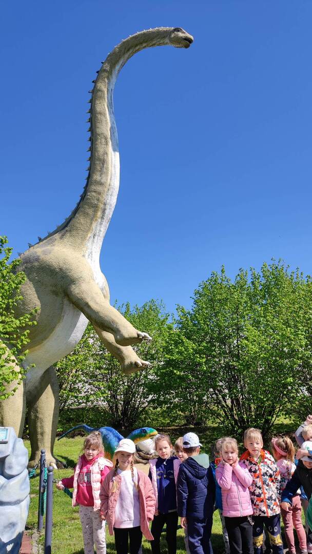 Dzieci pozują do zdjęcia, w tle figura dinozaura.