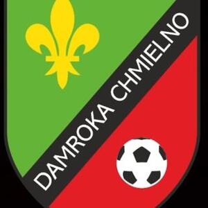 Logo Damroka Chmielno. Na czarnym tle proporzec w kolorach zielono czerwonym. Lewa część proporca zielona. Na zielonej części żółta lilijka. Przez środek, na ukos biały napis na czarnym tle Damroka Chmielno. Prawa część czerwona. Na czerwonej części piłka. 