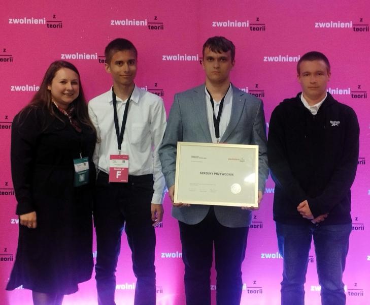 Uczniowie 2ET ZSCKP wraz z opiekunką projektu - Panią Pauliną Pabiańczyk na tle ścianki zdjęciowej Wielkiego Finału olimpiady Zwolnieni z Teorii