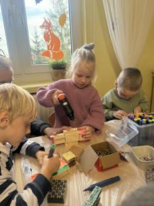 Dzieci uczestniczą w warsztatach stolarskich, wykonują ludziki z drewna.