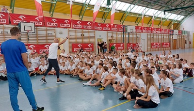 Grupa dzieci siedzi na hali sportowej