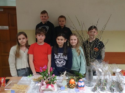 Uczniowie stojący przy stoliku z wielkanocnymi ozdobami.