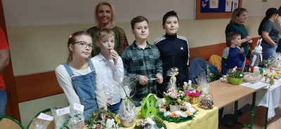 Uczniowie wraz z wychowawczynią stoją przy stoliku z wielkanocnymi ozdobami.