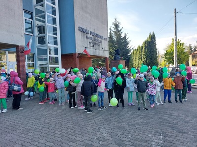 Uczniowie stojący przed budynkiem szkoły trzymają w rękach kwiaty z bibuły przygotowane na marsz z okazji Dnia Ziemi.