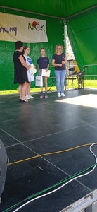 Grupa osób stojących na scenie. Uczennica trzymająca dyplom i upominek.