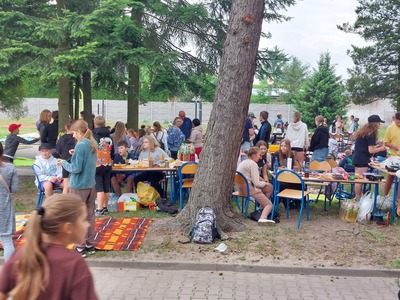 Grupa uczniów siedząca przy stolikach na terenie zielonym szkoły.