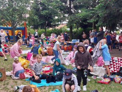 Uczniowie siedzą na kocach na terenie zielonym szkoły