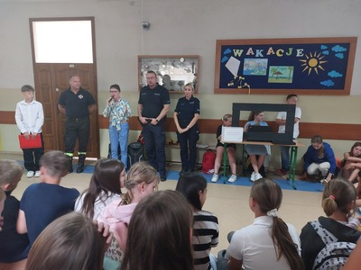 Korytarz szkolny.  Pani dyrektor dziękuje policjantom, strażakowi i uczniom uczestniczącym w apelu.