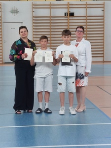 Hala sportowa. Dwoje  uczniów z klasy 4c stoi w szeregu, trzymając dyplomy. Obok nich stoi wychowawczyni  i dyrekcja szkoły..
