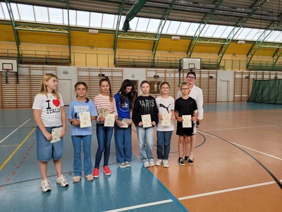 Hala sportowa. Grupa  uczniów z klasy 5a stoi w szeregu, trzymając dyplomy. Obok nich stoi dyrekcja szkoły..