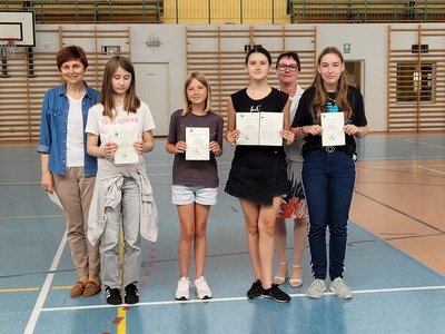 Hala sportowa. Grupa  uczniów z klasy 6b stoi w szeregu, trzymając dyplomy. Obok nich stoi wychowawczyni  i dyrekcja szkoły.
