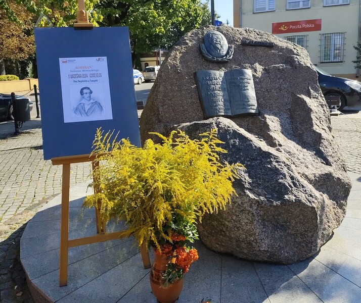 Pomnik Władysława Reymonta obok którego stoi na sztaludze afisz promujący wydarzenie: XIII edycja Narodowego Czytania "Kordiana" J. Słowackiego