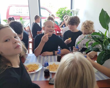 Uczniowie siedzą przy stolikach w Bistro "Tuszynianka" i jedzą frytki.