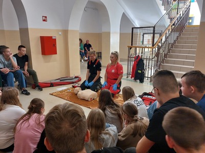 Strażak i ratownik medyczny prezentujący przed uczniami przygotowanie do resuscytacji.