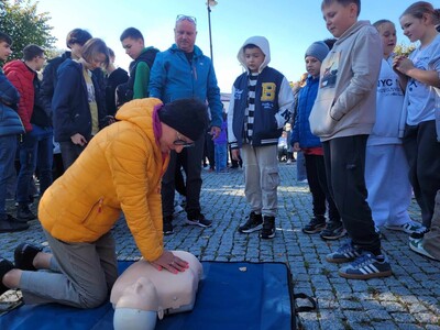 Pani Dyrektor w otoczeniu uczniów wykonująca masaż serca na fantomie. 