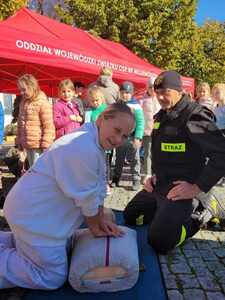 Uczennica pod nadzorem strażaka z OSP w Tuszynie wykonująca masaż serca na fantomie.
