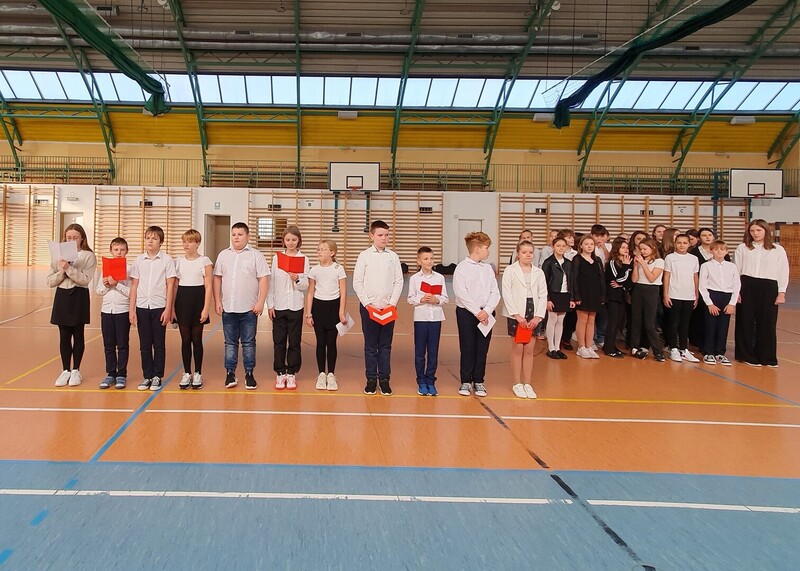 Uczniowie  w strojach galowych na hali sportowej.