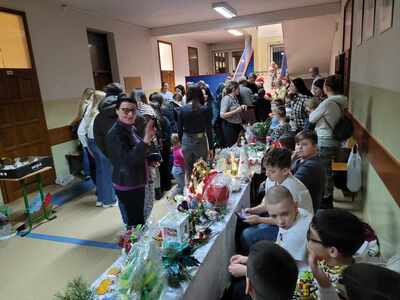 Korytarz szkolny na nimi stoiska z kiermaszowe wraz z osobami kupującymi.