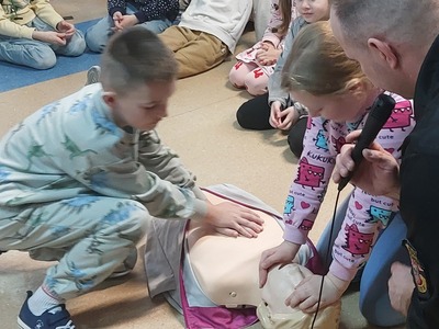 Uczeń przy wsparciu strażaka ćwiczy na fantomie masaż serca.