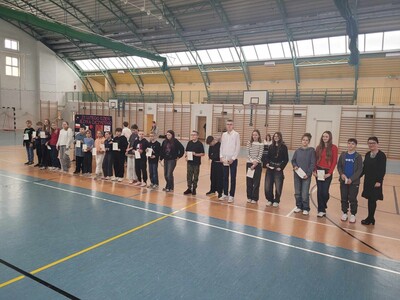 Uczniowie  uhonorowani dyplomami gratulacyjnymi za osiągnięcia edukacyjne i sportowe na hali sportowej  z panią dyrektor przed społecznością szkolną.