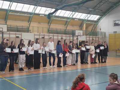 Uczniowie  uhonorowani dyplomami gratulacyjnymi za osiągnięcia edukacyjne i sportowe na hali sportowej  z panią dyrektor przed społecznością szkolną.