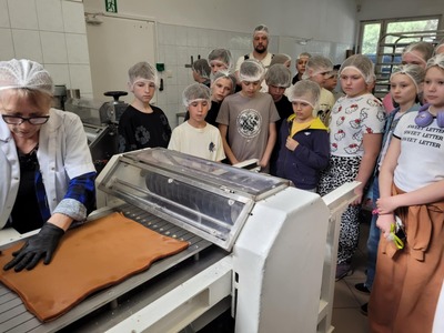 Uczniowie przyglądający się pracy cukiernika przy maszynie wyrabiającej masę na cukierki.