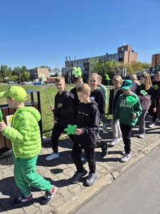 Uczniowie przemierzający ulice miast pod opieką nauczycieli trzymający zielone balony, chorągiewki oraz bibułowe kwiaty.