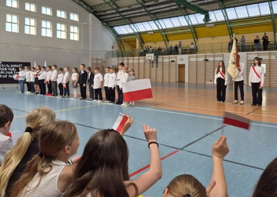 Uczniowie w strojach galowych występujący przed społecznością szkolną..