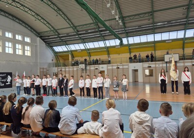 Uczniowie w strojach galowych występujący przed społecznością szkolną.
