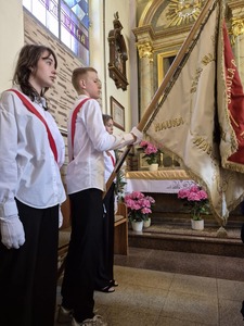 Uczniowie w strojach galowych ze sztandarem stojący w kościele,